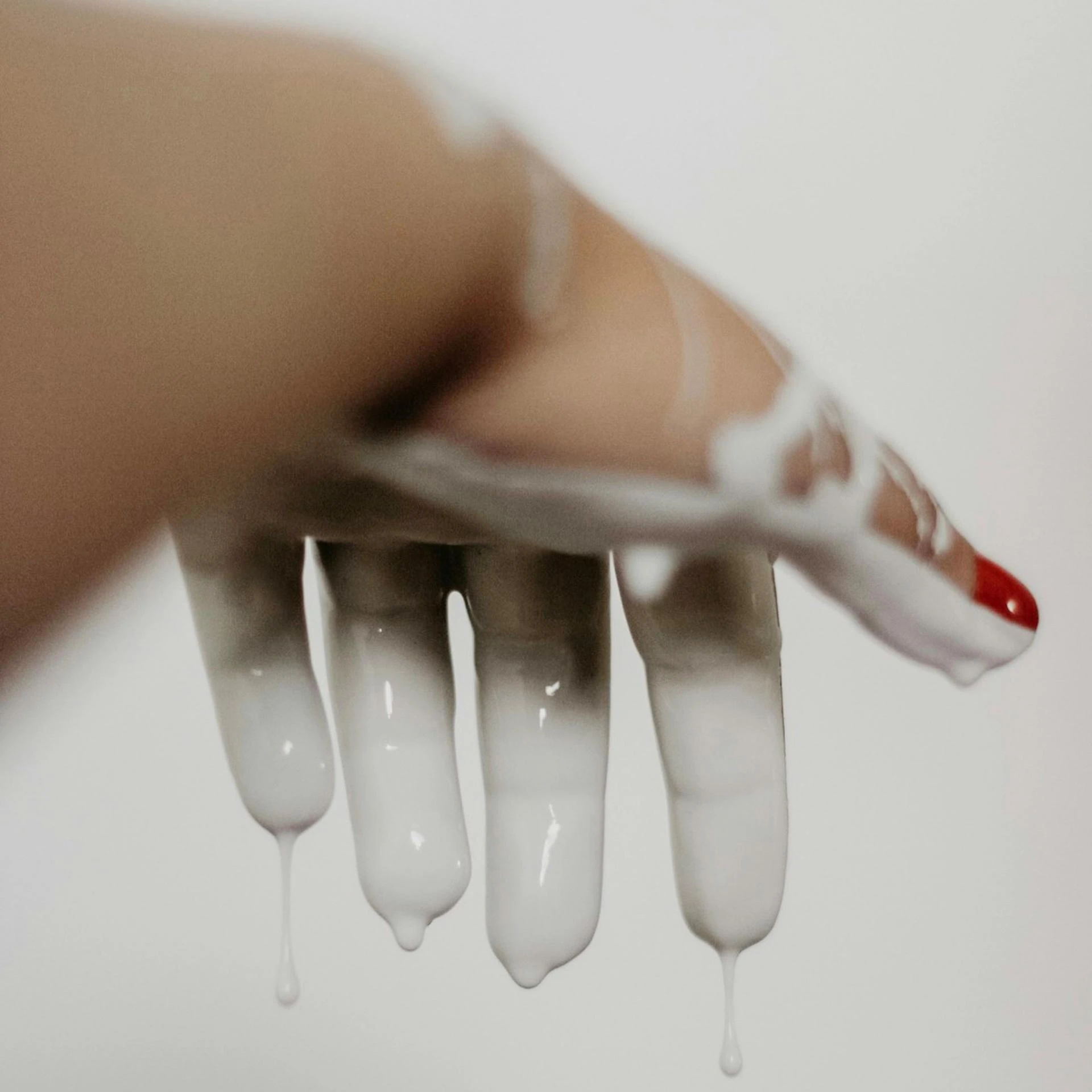 Inverted girl hand with red painted nail dripping with cream glue scaled