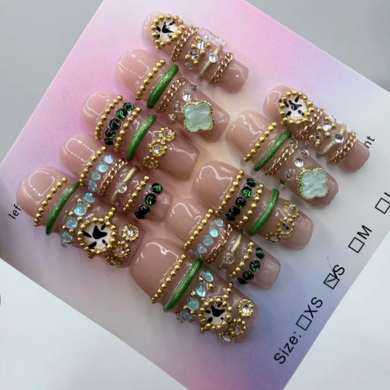 Handcrafted 3cm square press-on nails featuring a 3D bangle design with emerald green bands, gold chains, and clover charms on a nude base.