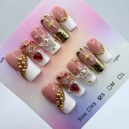 Handcrafted 2.5cm long square press-on nails with white French tips, 3D gold star charms, red heart crystals, and metallic gold bangle accents on a nude base.