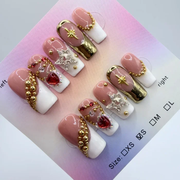 Handcrafted 2.5cm long square press-on nails with white French tips, 3D gold star charms, red heart crystals, and metallic gold bangle accents on a nude base.
