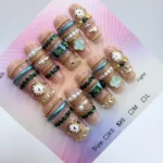 Handmade 3cm coffin press-on nails featuring gold bangle-style 3D art, pearls, watch face charms, and a mint green clover centerpiece on a nude base.